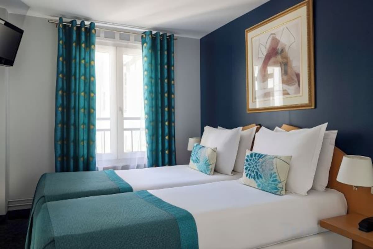 A hotel room with two beds, a television, a painting, and a window with curtains.