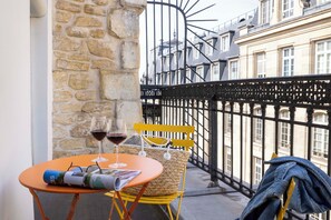 A balcony with a table, two glasses of red wine, a wicker basket, and a yellow chair. - Grand Hôtel du Calvados - Opéra (Paris)