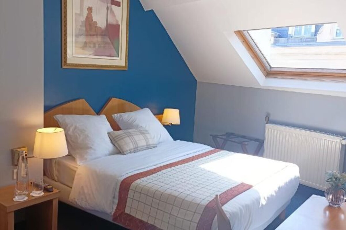A bedroom with a bed, two bedside lamps, a framed picture on the wall, and a skylight above the bed.
