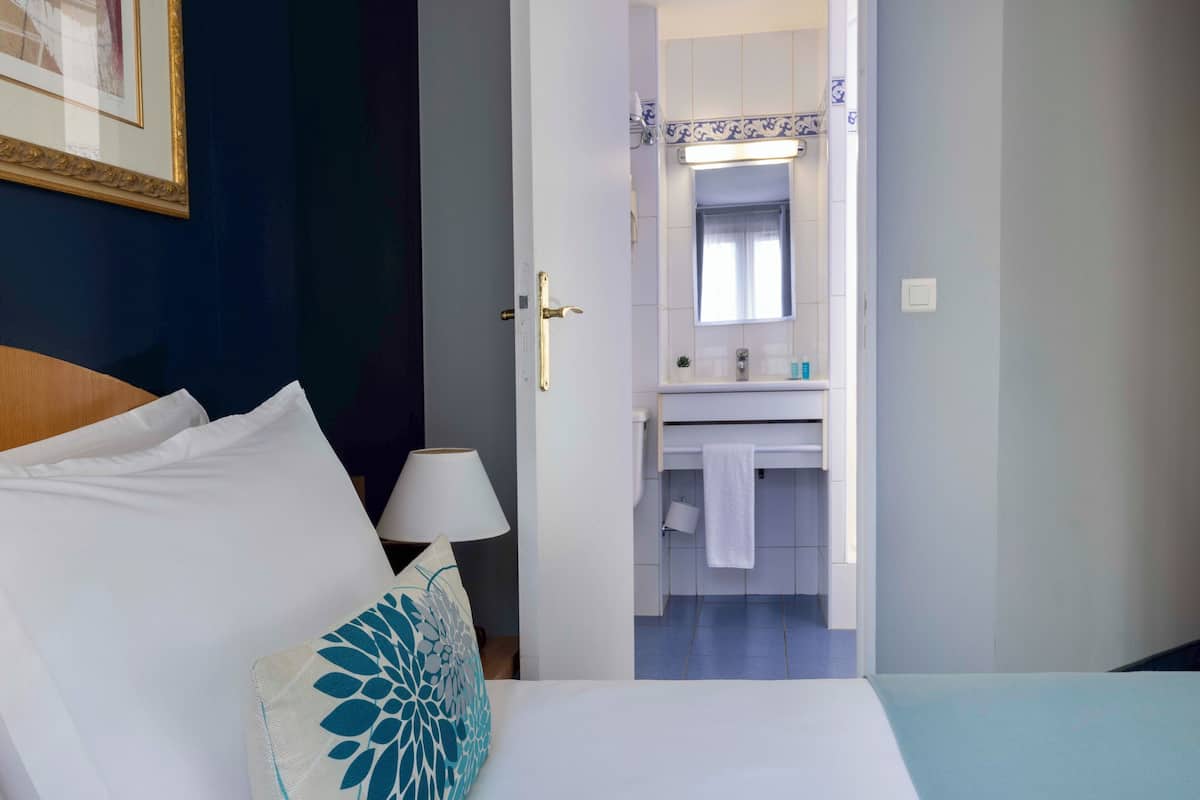 A hotel room with a bed, a nightstand, a lamp, a bathroom with a sink and mirror.