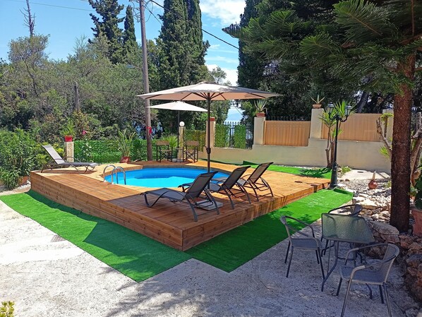 Una piscina rectangular amb un solàrium de fusta, envoltada d'herba sintètica verda, i equipada amb dos ombrel·les.