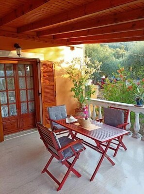 A wooden patio with a table and chairs, a glass door, and a view of greenery.