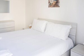 Cama bem arrumada com roupa de cama branca em um quarto simples e limpo.