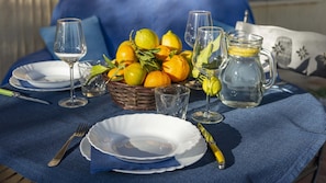 Una tavola imbandita con piatti, posate, un cesto di agrumi, bicchieri e una caraffa d'acqua.