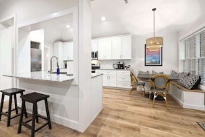 A modern kitchen with white cabinets, a granite countertop, and a dining area with a wooden table and chairs.