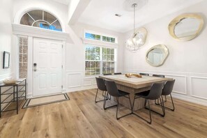 A dining area with a wooden table, four chairs, a chandelier, and a white door with a window above it.