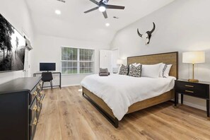 A bedroom with a bed, a desk, a chair, a lamp, and a ceiling fan.