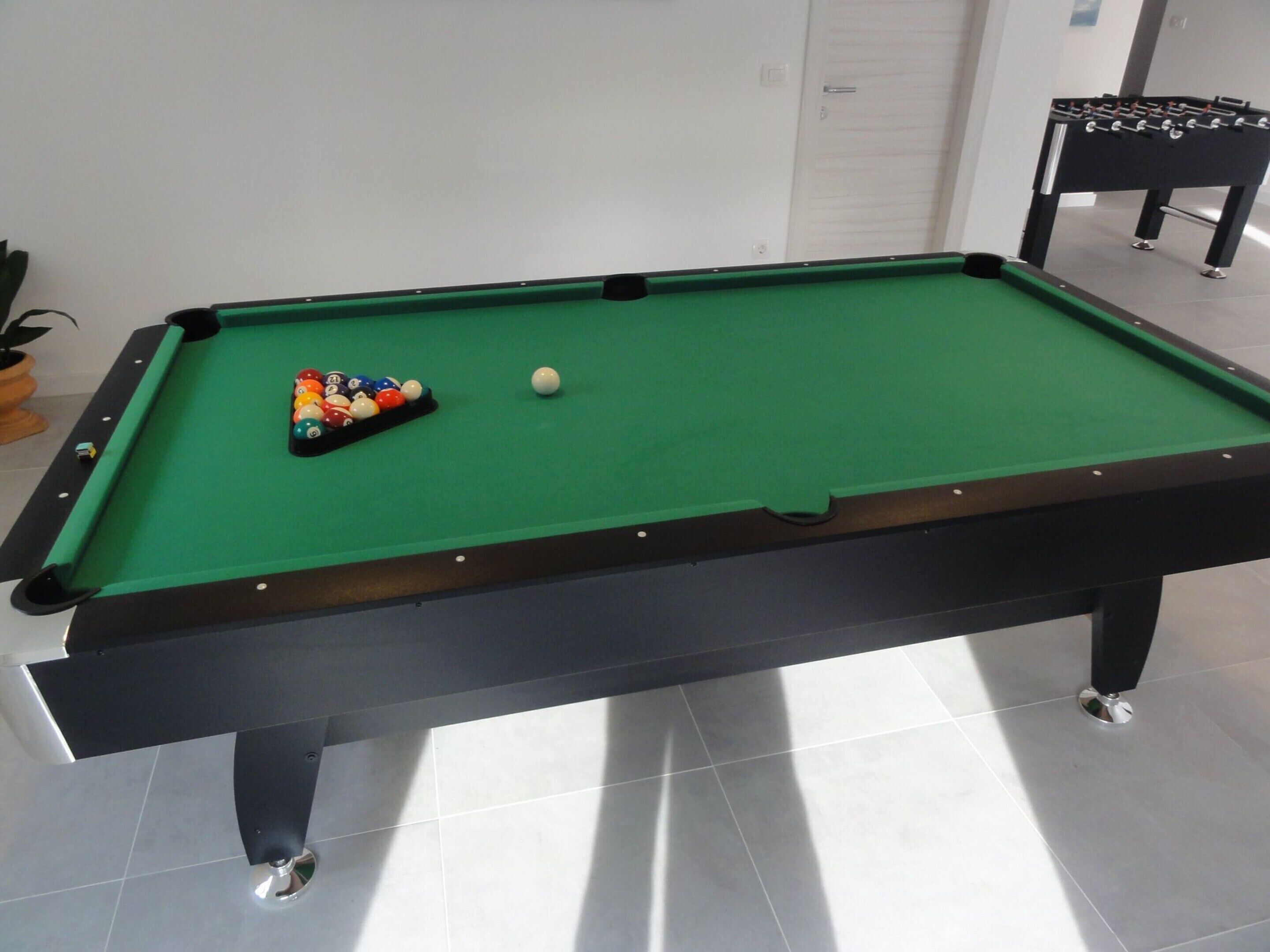 A pool table with balls and a foosball table in a room with tiled flooring.