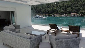 A balcony with wicker furniture, a glass table, and a view of a marina with boats. - Villa Riva - Five Bedroom Villa With Pool and Sea View (Dubrovnik)