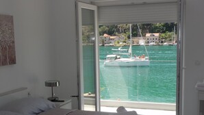 A bedroom with a bed, a nightstand, a lamp, and a view of a marina with boats. - Villa Riva - Five Bedroom Villa With Pool and Sea View (Dubrovnik)