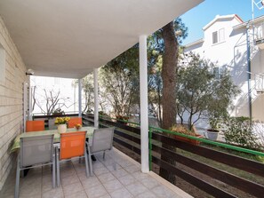 A covered outdoor seating area with a table and chairs, surrounded by trees and a staircase. - Apartments Pinija - Three Bedroom Apartment With Terrace - (Supetar)