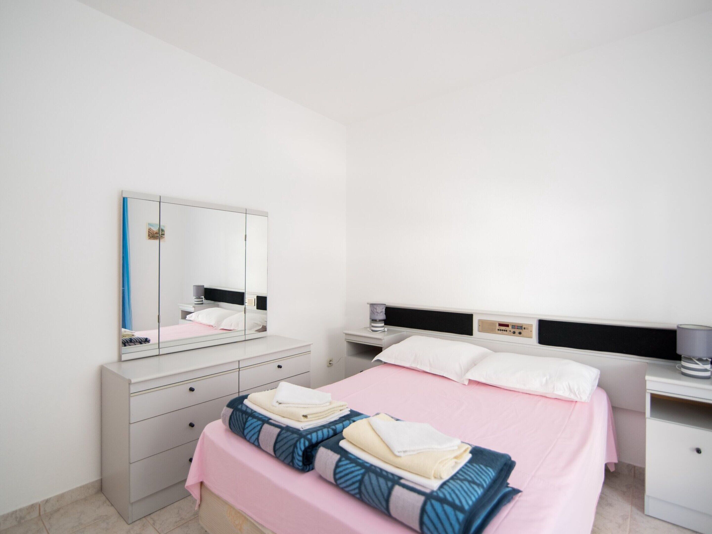 A modern hotel room with a bed, a bedside table, a mirror, and a wardrobe.