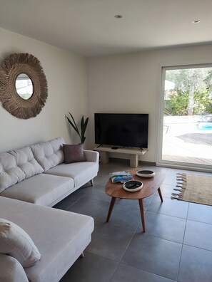Uma sala de estar com sofá, mesa de centro, televisão e uma janela ampla.
