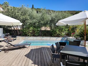 Um deck de madeira com piscina, espreguiçadeiras e guarda-sóis.