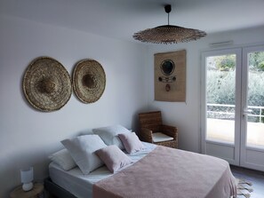 Quarto com cama, almofadas, cadeira de vime, luminária de palha no teto e tapeçaria na parede.