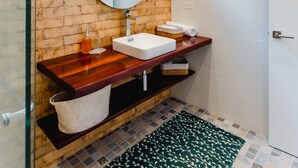 A bathroom with a wooden wall, a round mirror, a white sink, and a green patterned rug. - Casa Love 2B (Panama City)