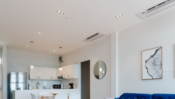 A modern kitchen with white cabinets and a central island, a dining area with a blue sofa and white chairs, and a wooden coffee table. - Casa Love 2B (Panama City)