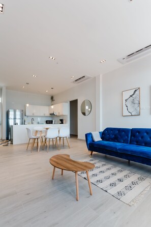 A modern kitchen with white cabinets and a central island, a dining area with a blue sofa and white chairs, and a wooden coffee table. - Casa Love 2B (Panama City)
