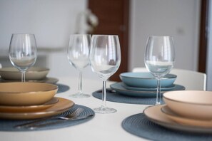 A dining table set with clear wine glasses, plates, and cutlery. - Welcomely - Xenia - Attico Mediterraneo (Olbia)