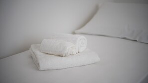 A neatly folded white towel on a bed with a white pillow. - Welcomely - Xenia - Attico Mediterraneo (Olbia)
