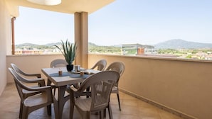 A balcony with a table and chairs, a potted plant, and a view of buildings and mountains.