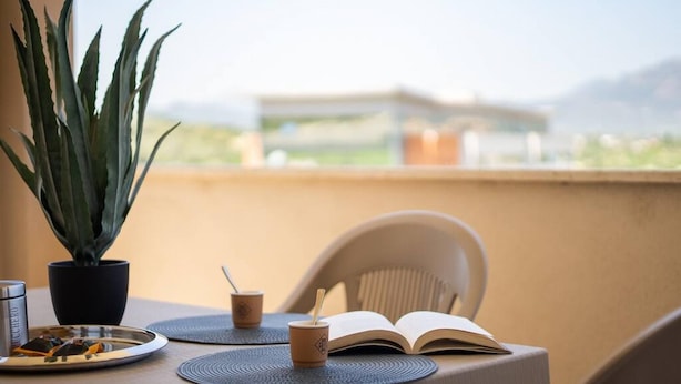 A balcony with a table set for a meal, a potted plant, and an open book.