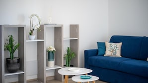 A modern living room with a blue sofa, white shelves, and small tables.