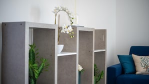 A modern living room with a blue sofa and a grey bookshelf with white flowers.