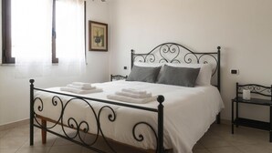 Ein ordentlich bezogenes Bett mit weißen Leinen und gefalteten Handtüchern, ein schwarzer Metall-Kopfteil, ein Nachttisch mit Lampe und ein gerahmtes Bild an der Wand.