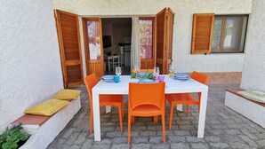 An outdoor dining area with a table set for four, surrounded by orange chairs, and wooden shutters on the windows. - Welcomely - La Casa Di Rita - Salamaghe (Budoni)