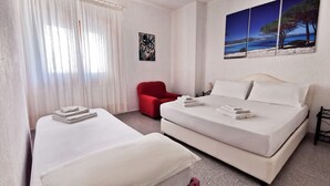 A hotel room with two beds, a red chair, a painting of a beach, and a lamp. - Welcomely - La Casa Di Rita - Salamaghe (Budoni)