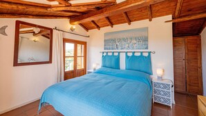 A bedroom with a wooden ceiling, a bed with a blue bedspread, a nightstand with a lamp, and a door with a wooden door. - Welcomely - Le Vele in Olbia (Olbia)
