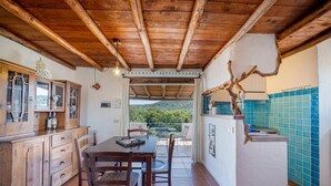 A rustic kitchen with wooden cabinets and a dining area with a table and chairs. - Welcomely - Le Vele in Olbia (Olbia)