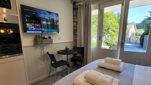 Moderni hotellihuone, jossa on sänky, seinälle asennettu televisio, pieni ruokapöytä ja näkymä ulos.
