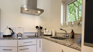 Moderni keittiö, jossa on valkoiset kaapit, ruostumattomasta teräksestä valmistettu liesituuletin, sisäänrakennettu uuni, pesuallas ja ikkuna, josta avautuu näkymä vehreään maisemaan.