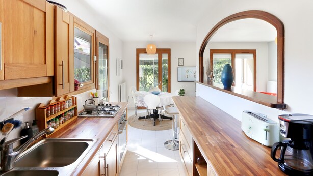 Een keuken met houten kastjes, een spoelbak, een fornuis en een eethoek met een tafel en stoelen.
