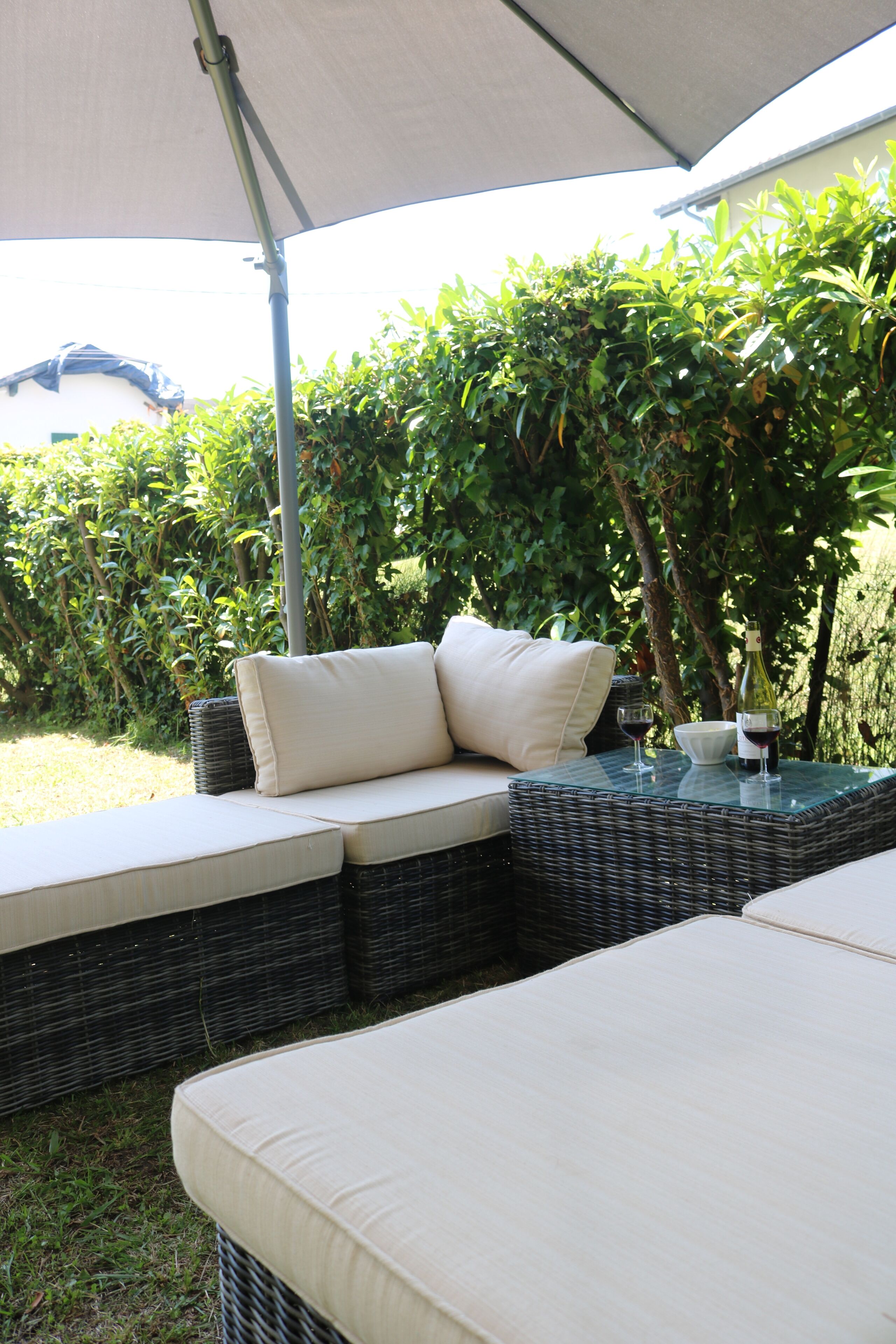 An outdoor seating area with a canopy, cushioned benches, and a glass table with a bottle and glasses.