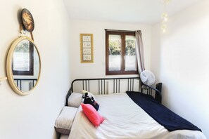Una camera da letto con un letto, un comodino, uno specchio, una finestra con tende e un ventilatore a parete.
