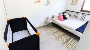 Een kamer met een ledikant, een bed met kussens, een kleine ronde tafel, een spiegel en een kamerkleed met dessin.