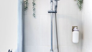 Een douche met een handdouche en een slangdouche, een zeepdispenser en een handdoekhouder.