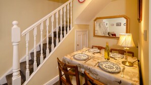 A dining area with a table set for two, a wooden chair, a mirror, and a staircase with white balusters. - 2 Bridge Syke, Elterwater (Ambleside)