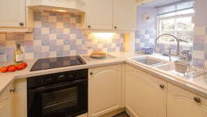 A kitchen with white cabinets, a checkered backsplash, a built-in oven, a stovetop, and a window with a view. - 2 Bridge Syke, Elterwater (Ambleside)