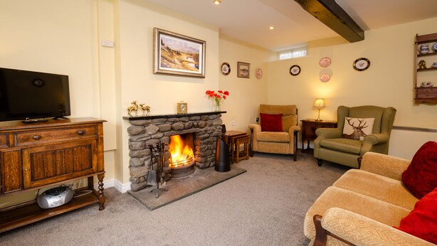 A cozy living room with a stone fireplace, a television, and a comfortable seating area. - 2 Bridge Syke, Elterwater (Ambleside)