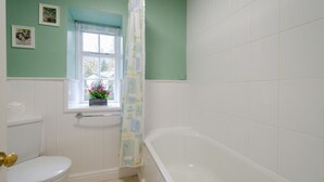 A bathroom with a white toilet, a window with a view, a bathtub, and a shower curtain. - 2 Bridge Syke, Elterwater (Ambleside)