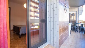 A modern interior with a sliding glass door leading to a balcony, a small bed, and a dining area with chairs and a table.