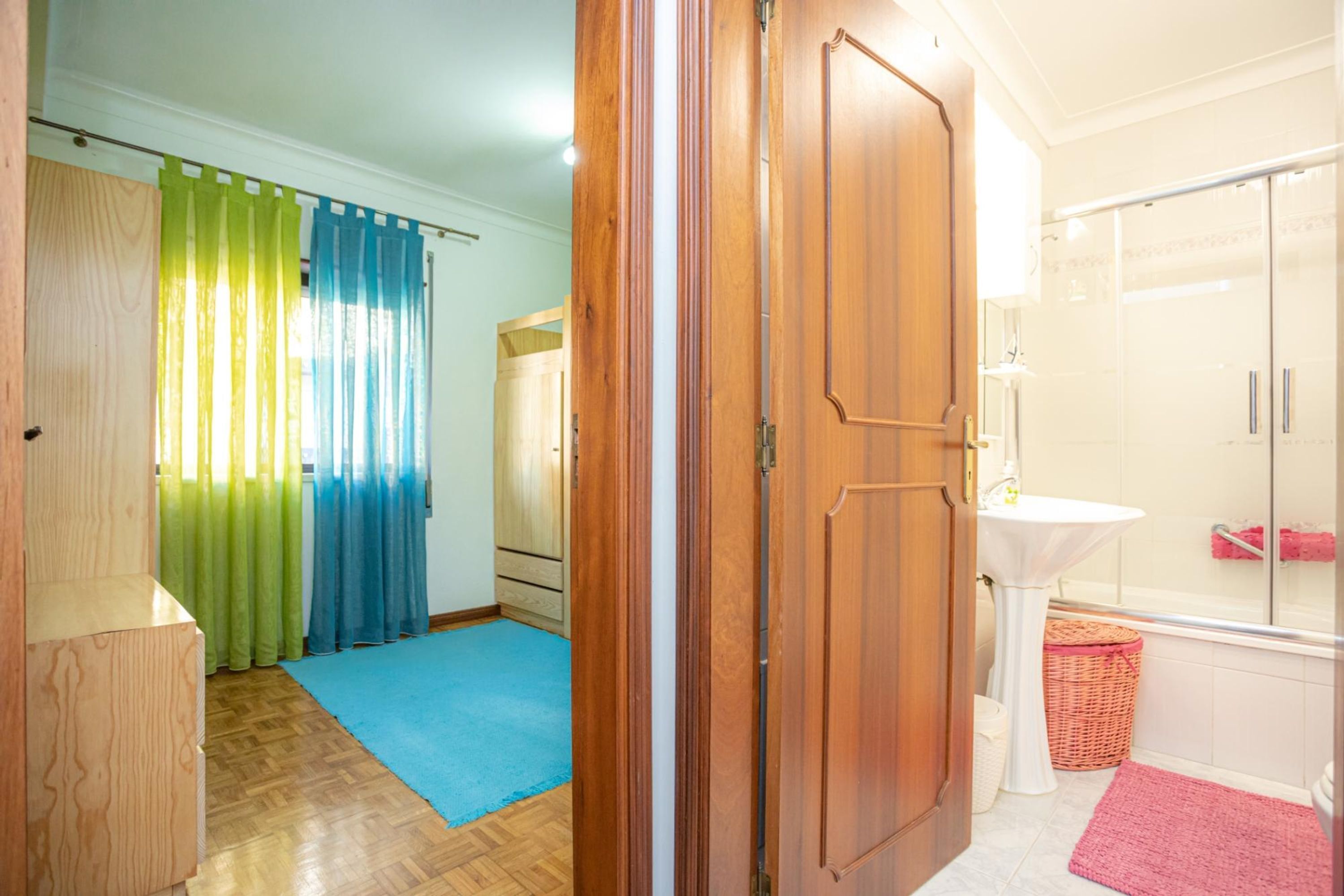 Une pièce avec une armoire en bois, une moquette bleue, une porte en bois, un lavabo blanc et une douche en verre.