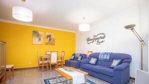 A living room with a blue sofa, a wooden coffee table, and a dining area with chairs and a table.