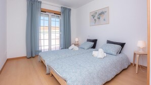 Een slaapkamer met een groot bed, twee nachtkastjes, een kaart aan de muur en een raam met gordijnen.