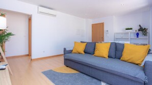 Een moderne woonkamer met een grijze bank, gele kussens, een houten vloer en een witte muur.