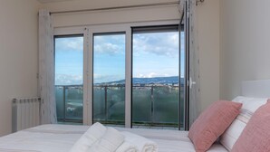 Habitación de hotel con una cama grande, vista de la ciudad a través de un ventanal y balcón con barandilla.